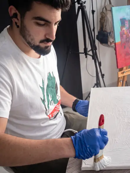 Artista con guantes azules sujetando un pincel frente a un lienzo en blanco